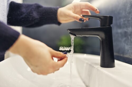 Image Text: woman rinsing invisalign aligners for Invisalign care